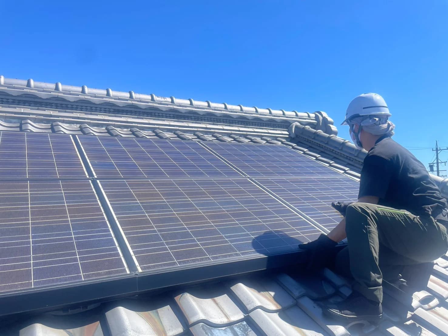 戸建て住宅の屋根上で太陽光パネルを点検する技術者